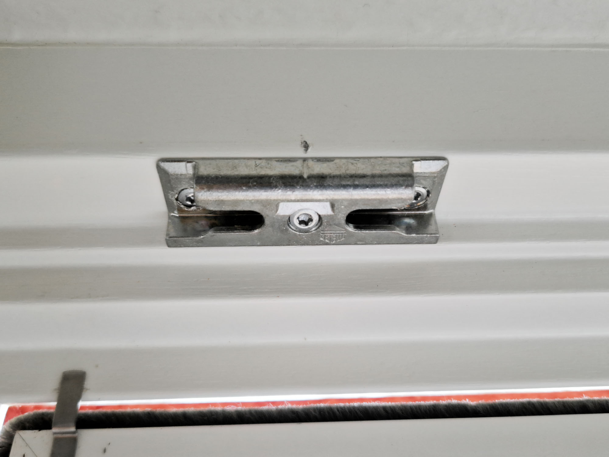 Detaillierte Ansicht einer Türschließe aus Metall, montiert an einer Holztür, zeigt Mechanismus und Sicherheitsmerkmale.